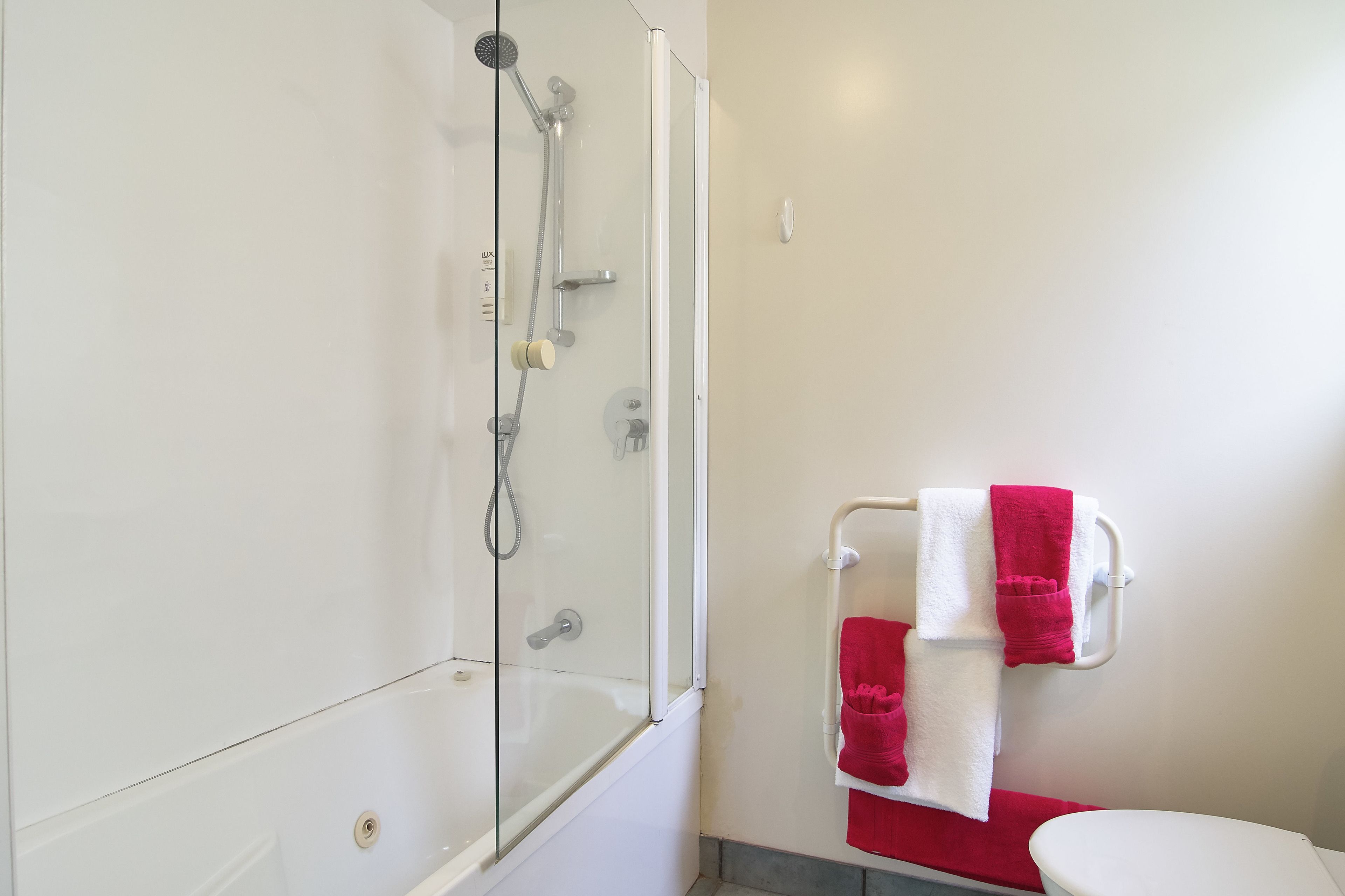 A bathroom with a glass-enclosed shower, a white toilet, and a towel rack with red and white towels.
