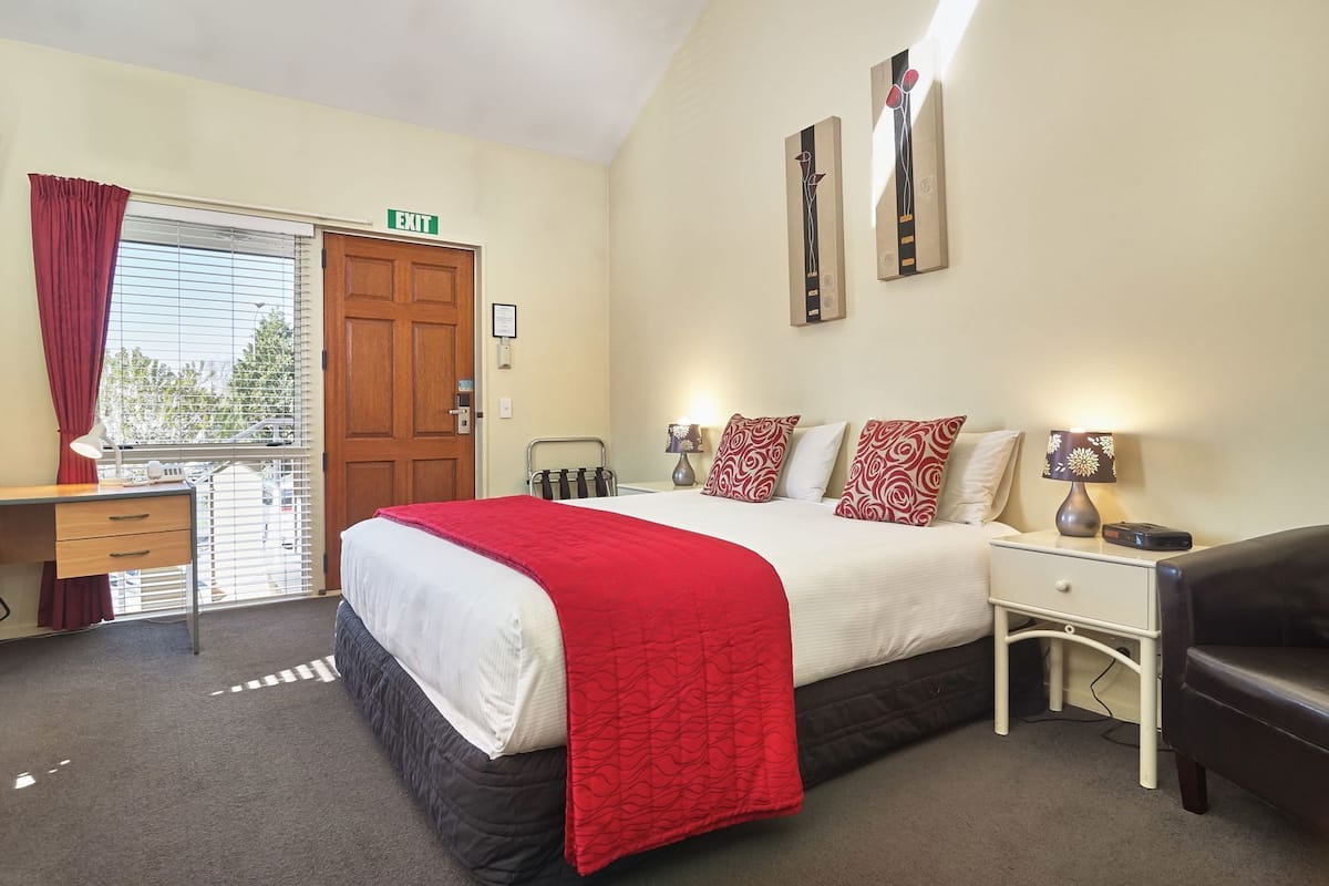 Une chambre d’hôtel avec un lit, des tables de chevet, un bureau et une porte de sortie.