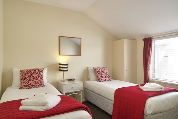 A hotel room with two beds, a nightstand with a lamp, a mirror, and a window with curtains. - Apollo Motel Christchurch (Christchurch)
