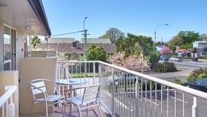 Ein Balkon mit Metallstühlen und einem Tisch, der auf eine Straße mit Autos und Bäumen blickt.