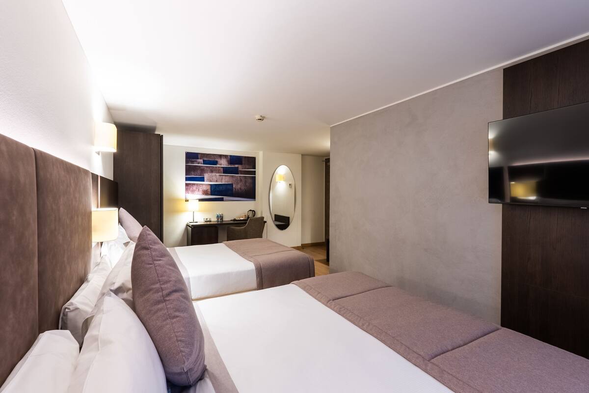 Une chambre d’hôtel avec deux lits, un bureau, une télévision et un miroir fixé au mur.