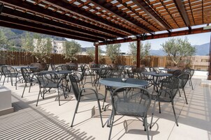 An outdoor patio with round tables and chairs, a wooden pergola, and a view of a mountainous landscape.