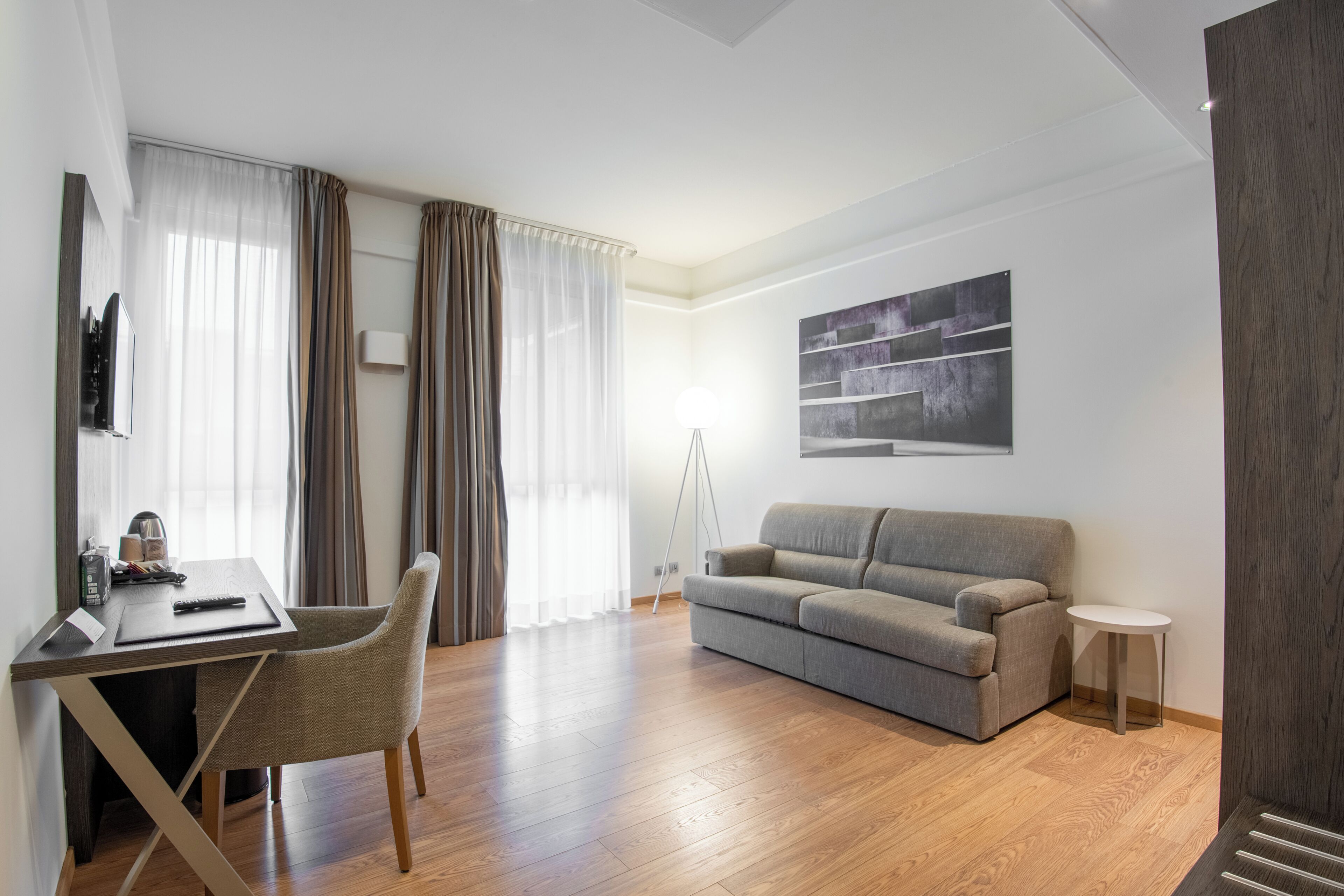 Una sala moderna con sofá, una mesa de comedor con sillas, una lámpara y un cuadro en la pared.