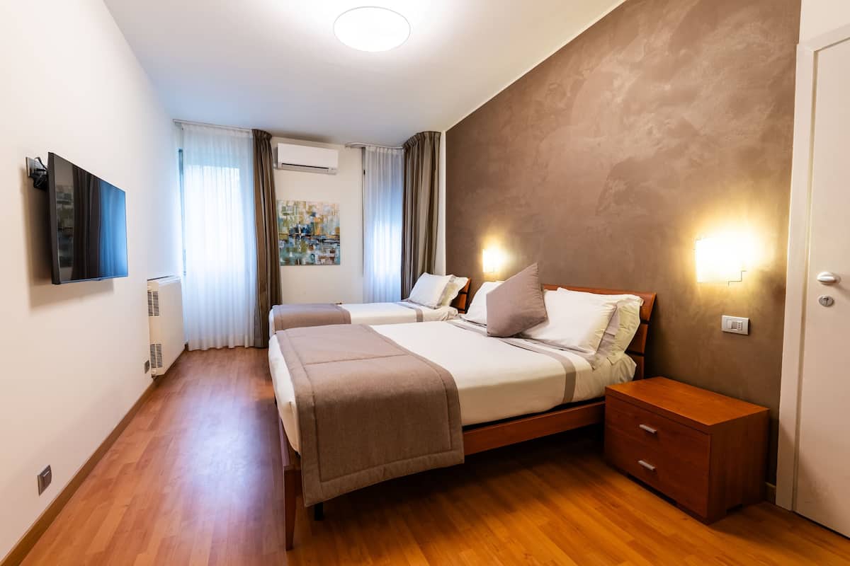 Une chambre d’hôtel moderne équipée de deux lits, d’un téléviseur à écran plat, d’une table de chevet et d’une lampe fixée au mur.
