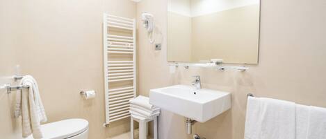 Baño con inodoro, lavamanos, toallero y espejo.