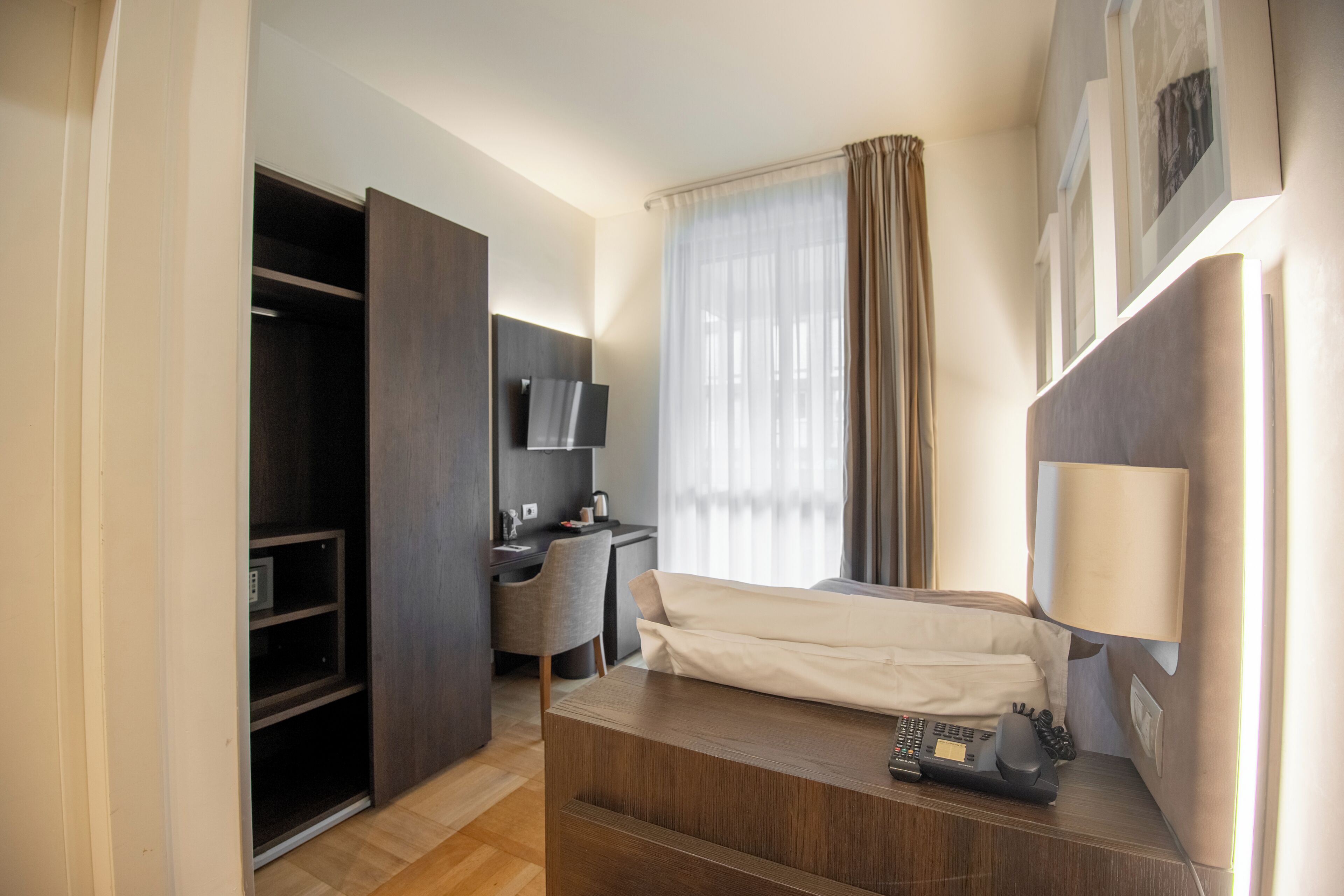 A hotel room with a bed, a desk, a chair, a wardrobe, a TV, and a window with curtains.