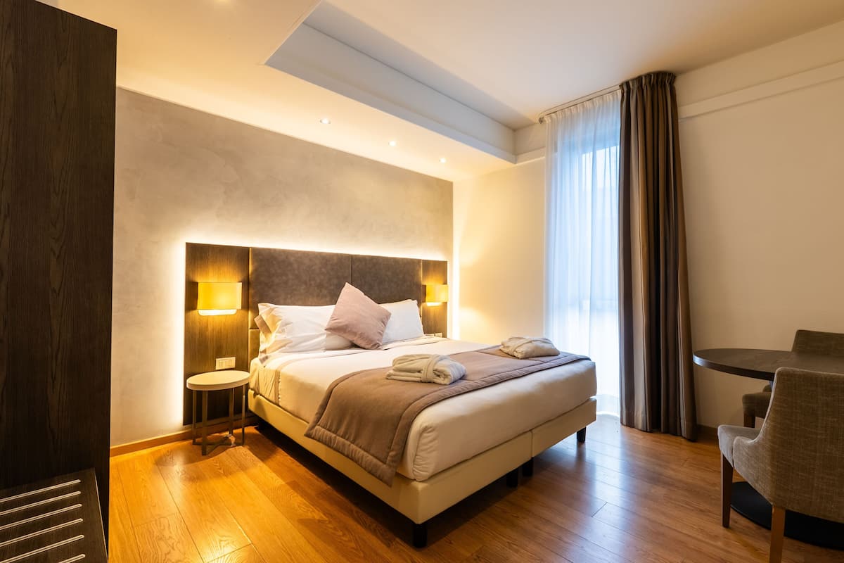Une chambre d’hôtel moderne dotée d’un grand lit, de tables de chevet, d’une table à manger ronde et offrant une vue sur l’extérieur.