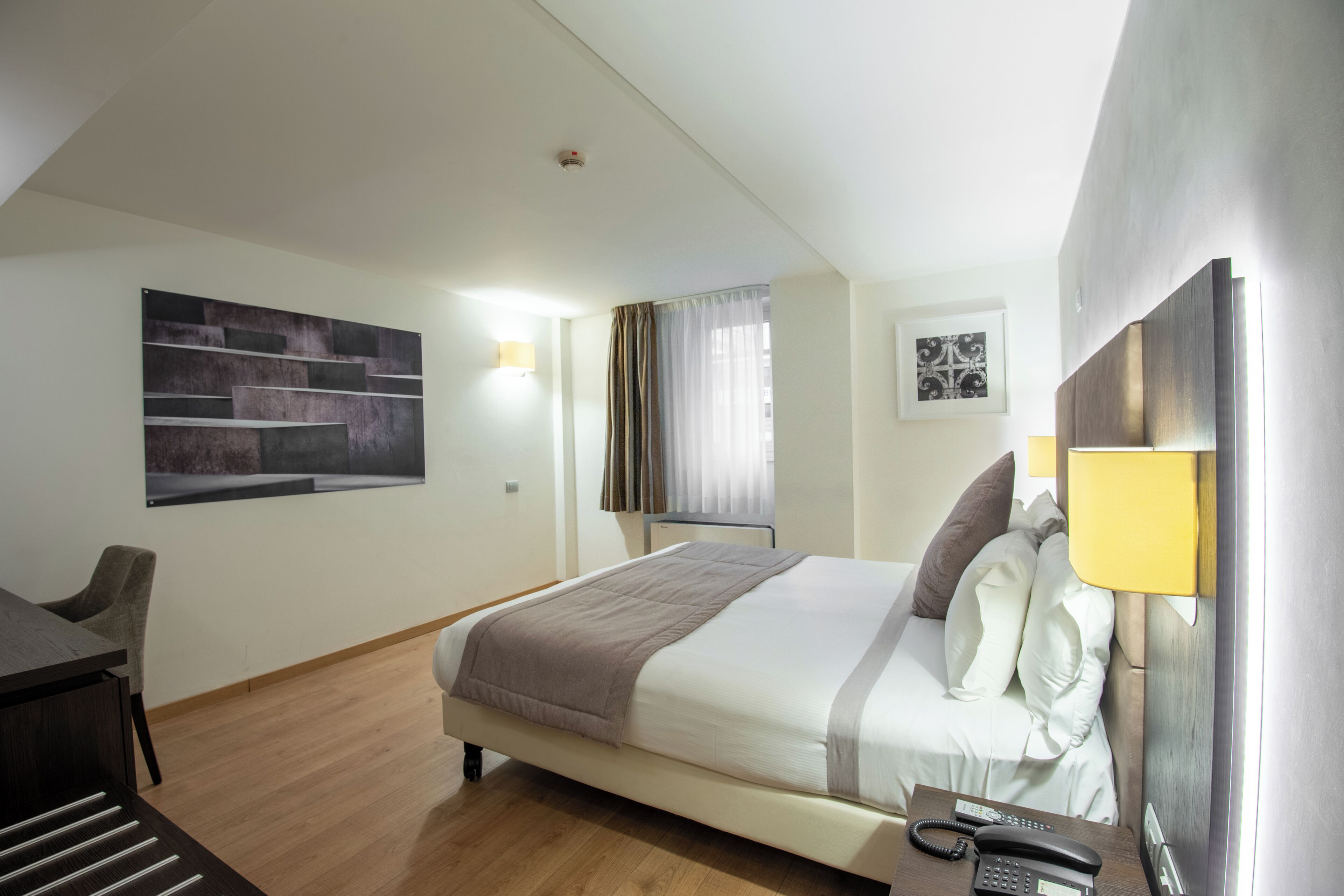 Una habitación de hotel con cama, mesita de noche, lámpara y un cuadro en la pared.