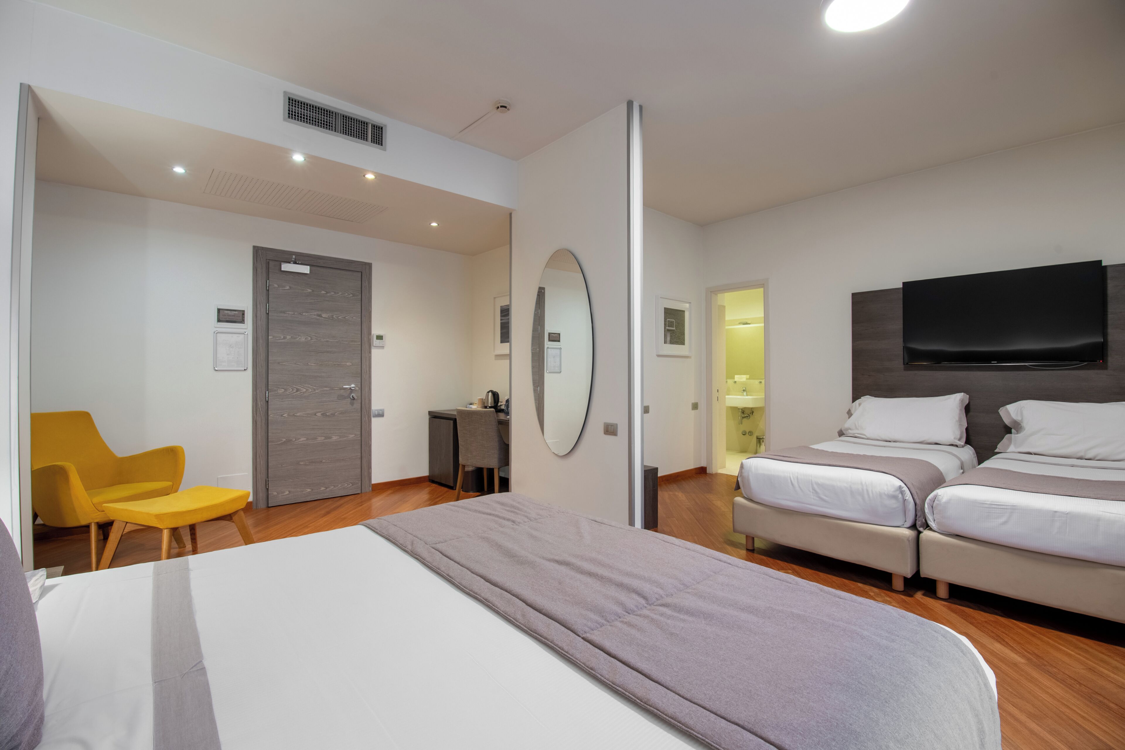 Habitación de hotel con cama, dos mesitas de noche, escritorio, silla, televisión y espejo.