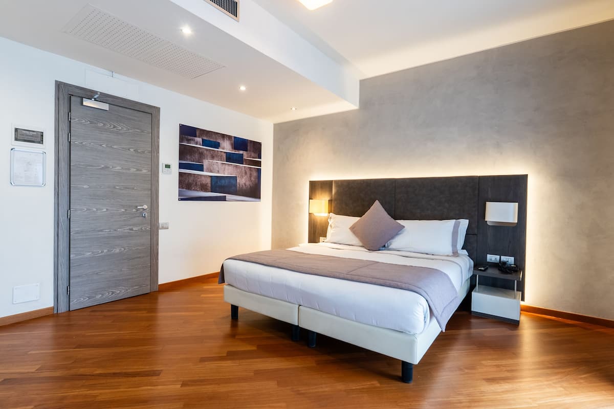 Une chambre moderne avec un grand lit, une table de chevet, une lampe fixée au mur et une porte en bois.