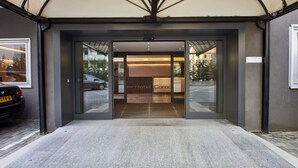 A hotel entrance with a glass door, a car parked outside, and a stone-tiled entrance area.