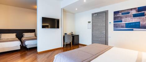 A modern hotel room with a large bed, two smaller beds, a desk, and a TV.