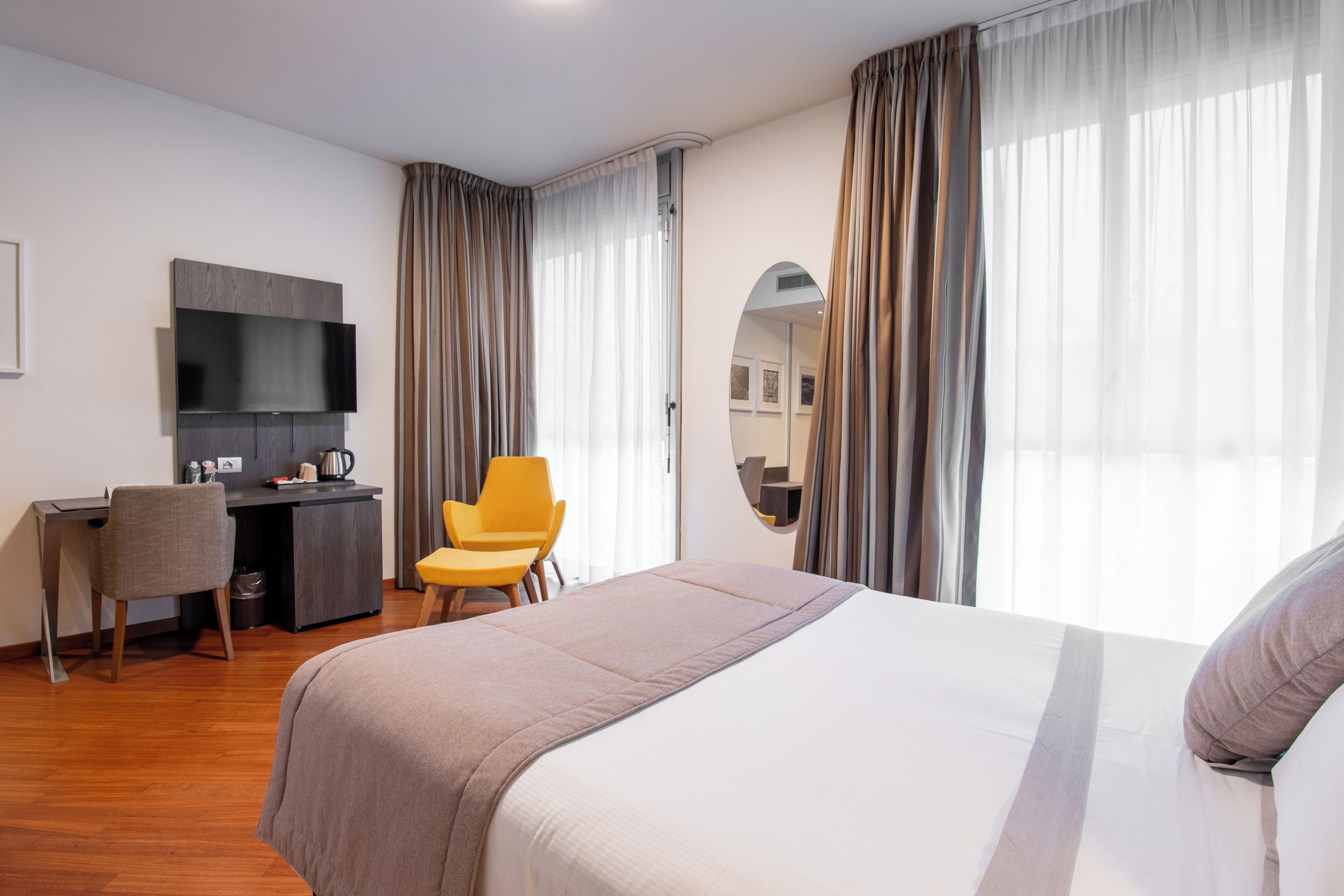 A hotel room with a bed, a desk, a chair, a television, and a large window with curtains.