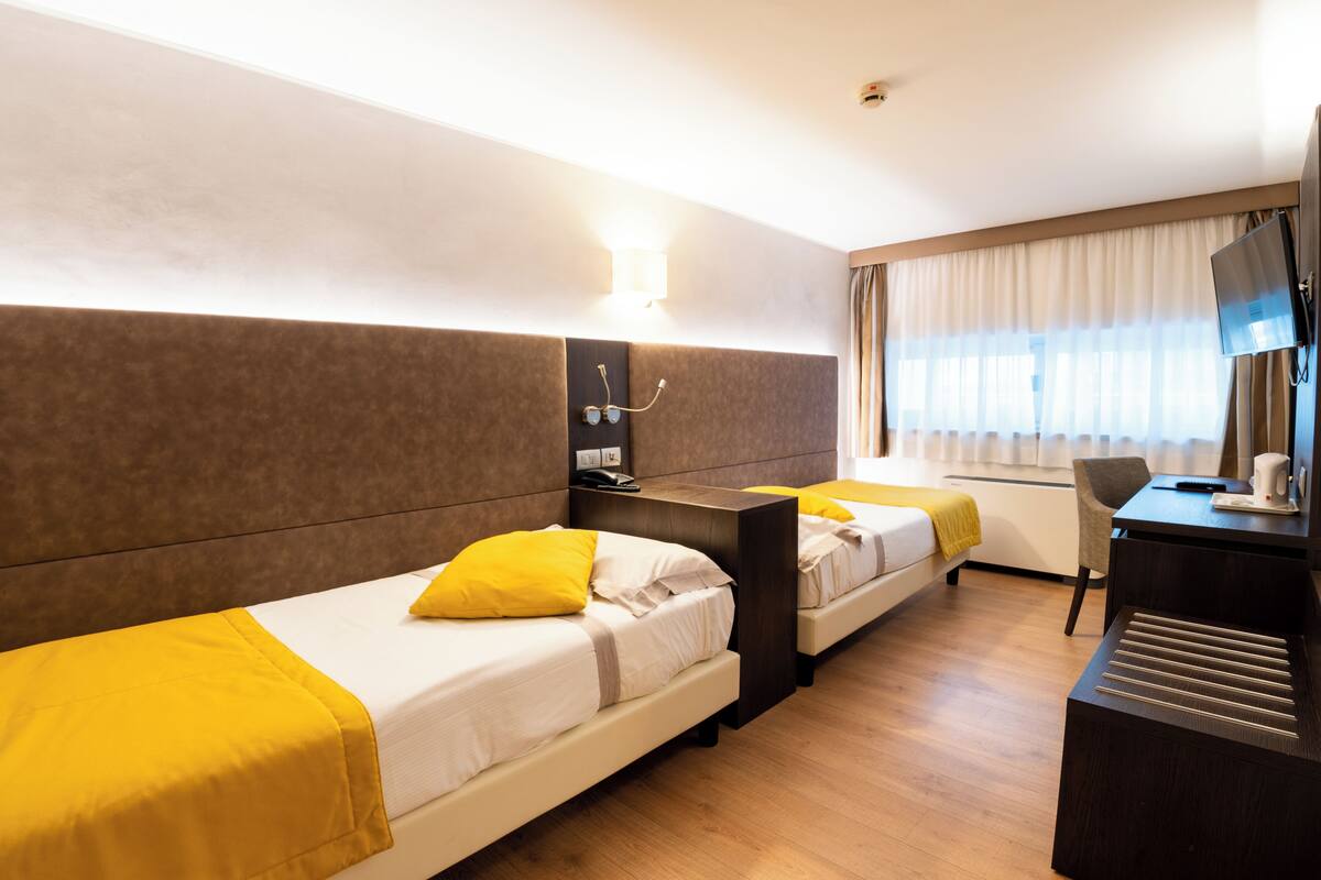 Une chambre d’hôtel avec deux lits, un bureau, une télévision et une fenêtre avec des rideaux.