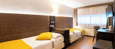 A hotel room with two beds, a desk, a TV, and a window with curtains.