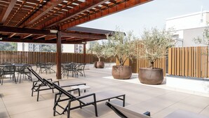 An outdoor patio with metal chairs and tables, large potted plants, and a wooden pergola structure.
