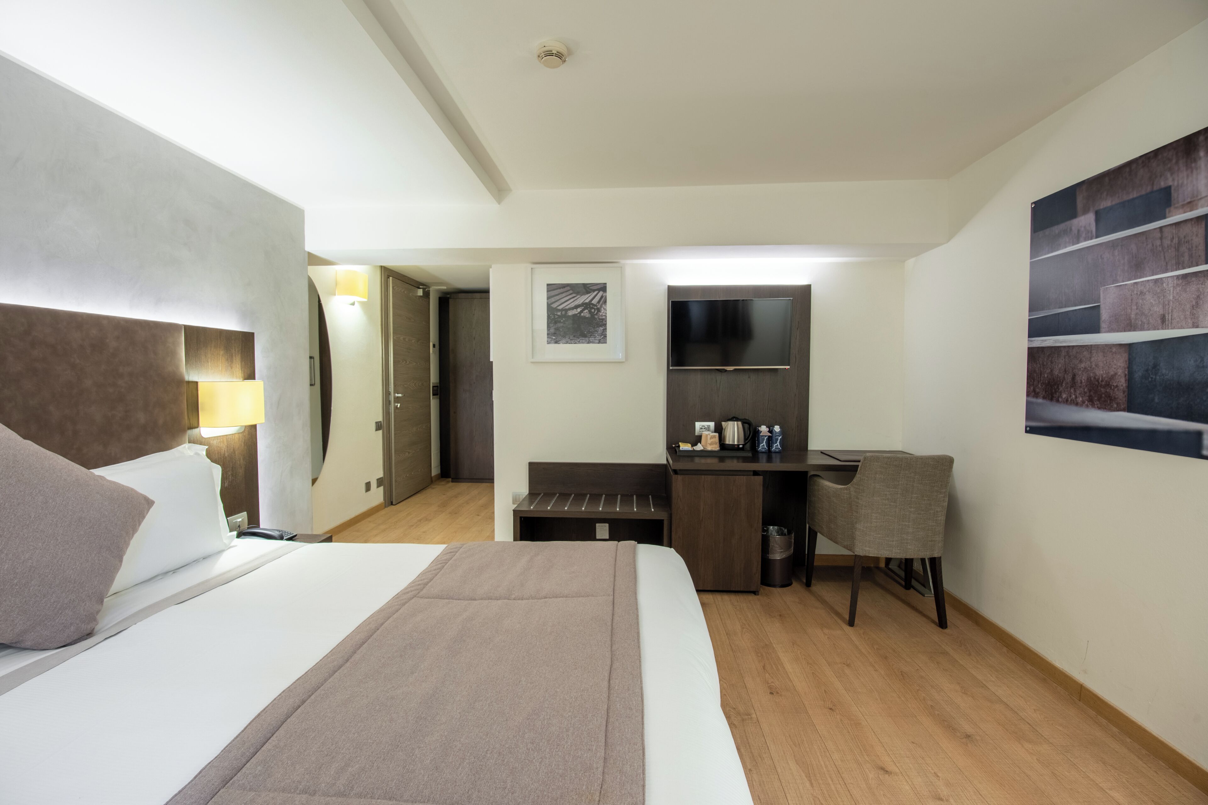 A hotel room with a bed, a desk, a chair, a TV, and a picture on the wall.
