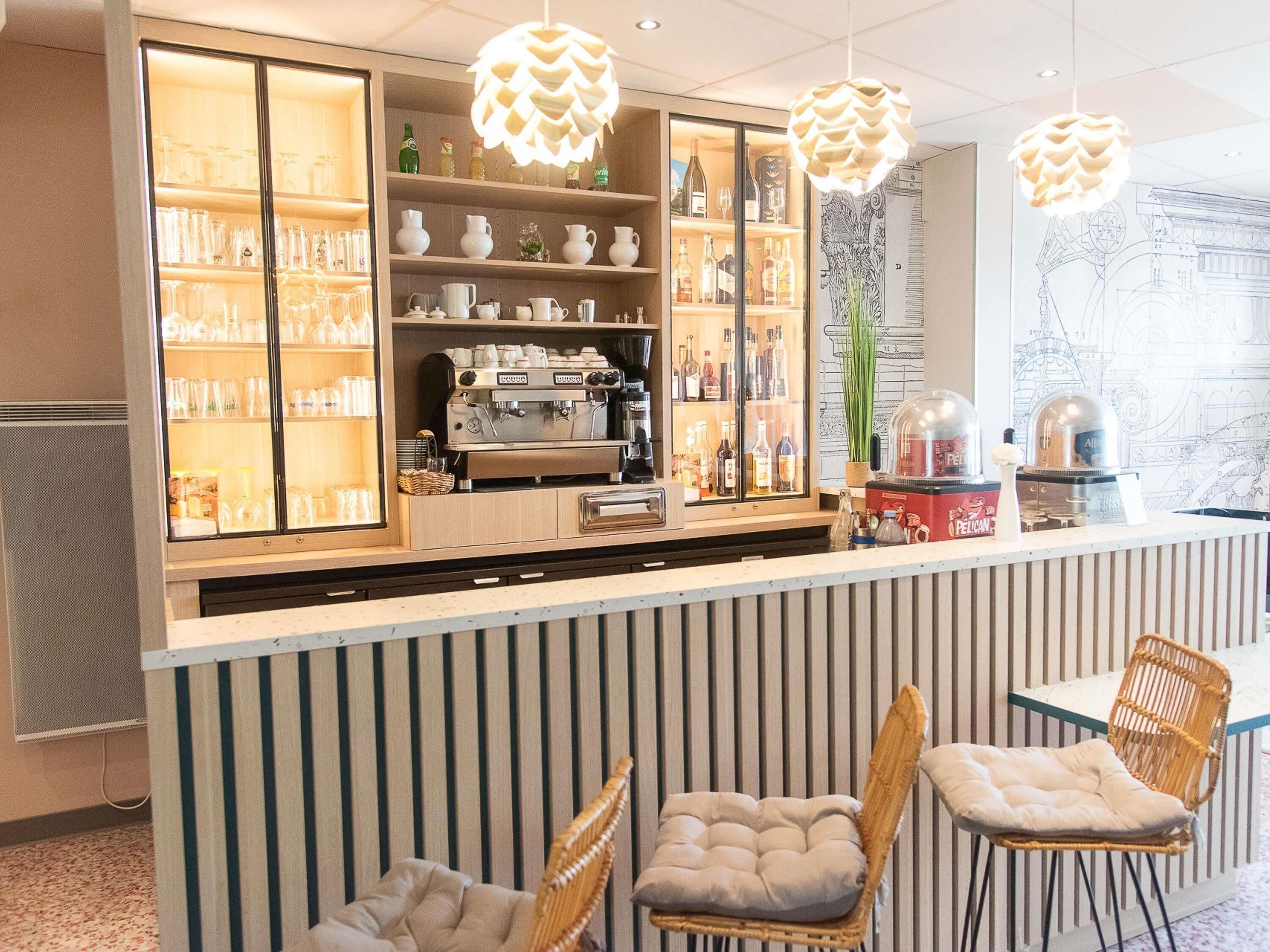 A bar area with shelves of glasses and bottles, a coffee machine, and wicker chairs.