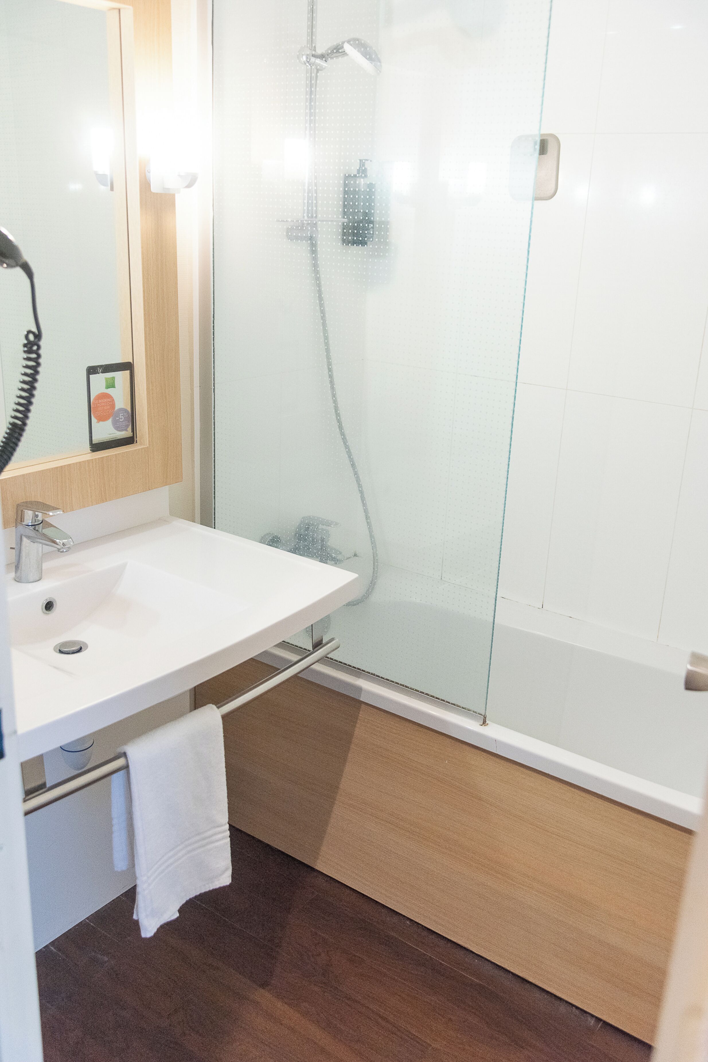Un baño con ducha de vidrio, lavamanos blanco y tocador de madera.