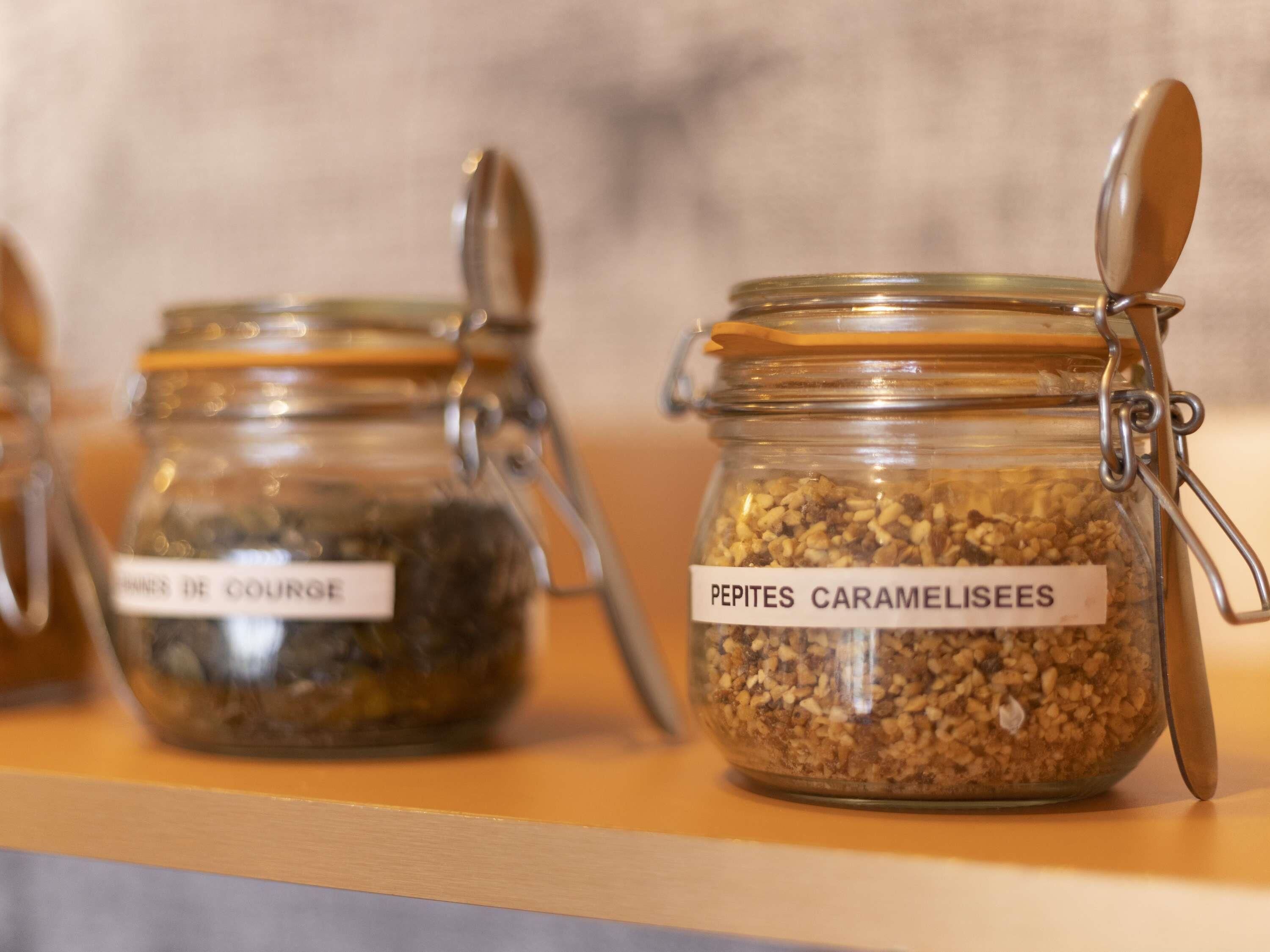 Två glasburkar med metallock och etiketter, den ena märkt med "PEPITES CARAMELISEES" och den andra med "PEPITES DE COURGE", placerade på en träyta.