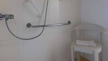 Een badkamer met een douche, een handgreep en een witte stoel met een handdoek.