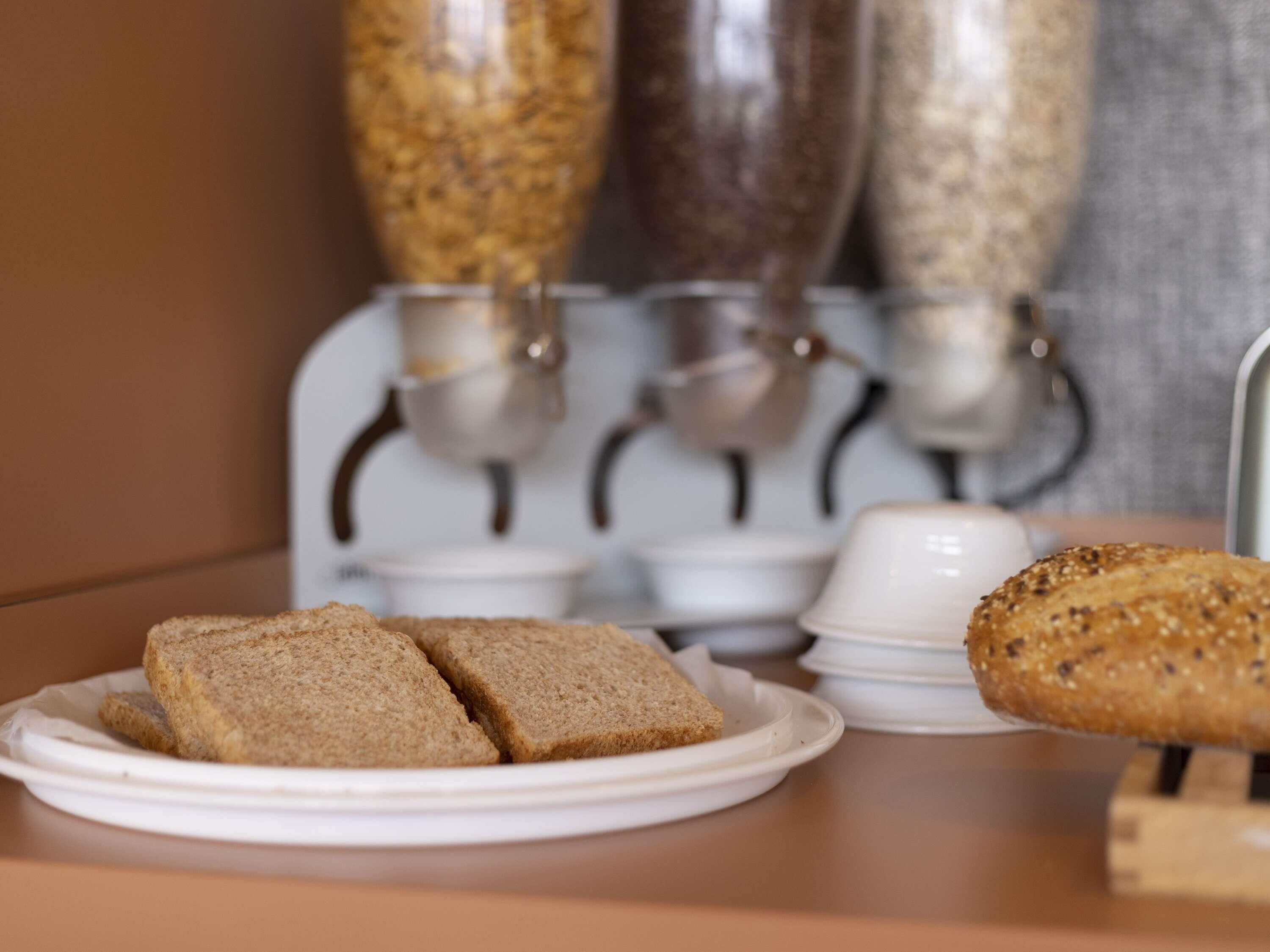 A breakfast setting with a plate of sliced bread and a whole loaf, a coffee machine, and a container of cereal.