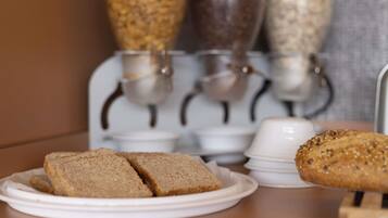 A breakfast setting with a plate of sliced bread and a whole loaf, a coffee machine, and a container of cereal.