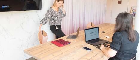 Una sala de conferencias con una mesa de madera, dos portátiles, un teléfono inteligente y una funda para portátil roja y negra.