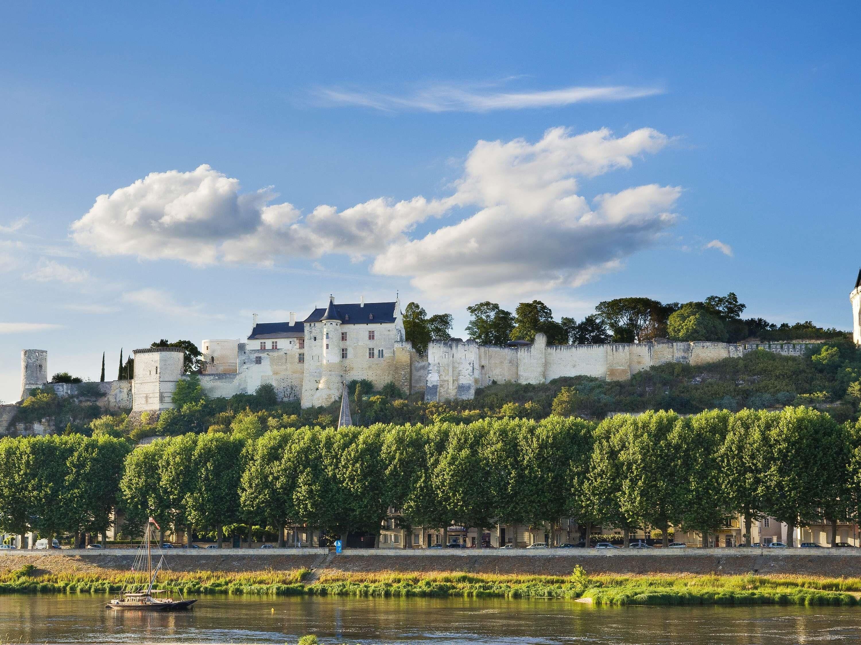 A historic castle with a river in the foreground and a clear sky.