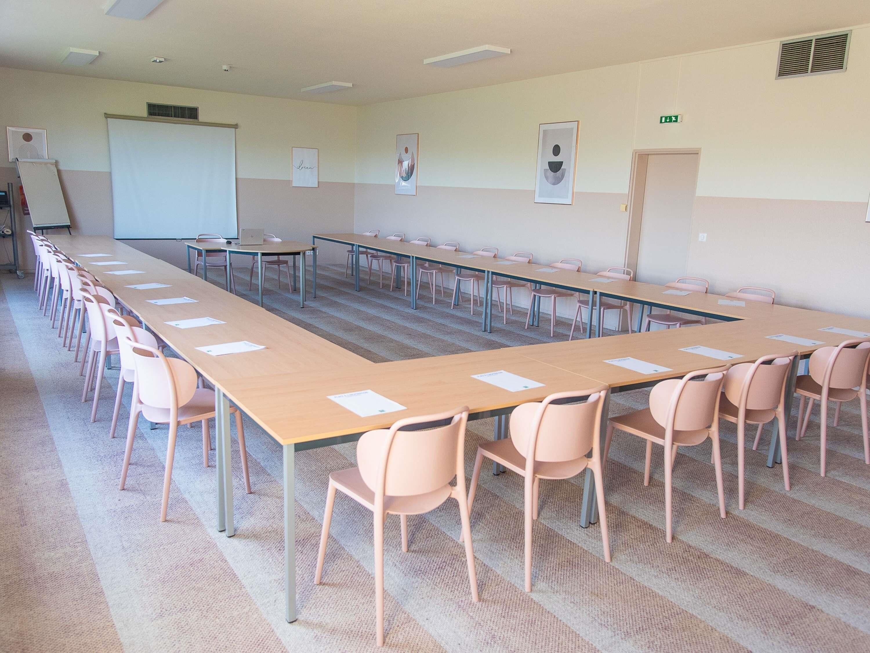 Un salón de conferencias con largas mesas y sillas, una pizarra y cuadros en las paredes.