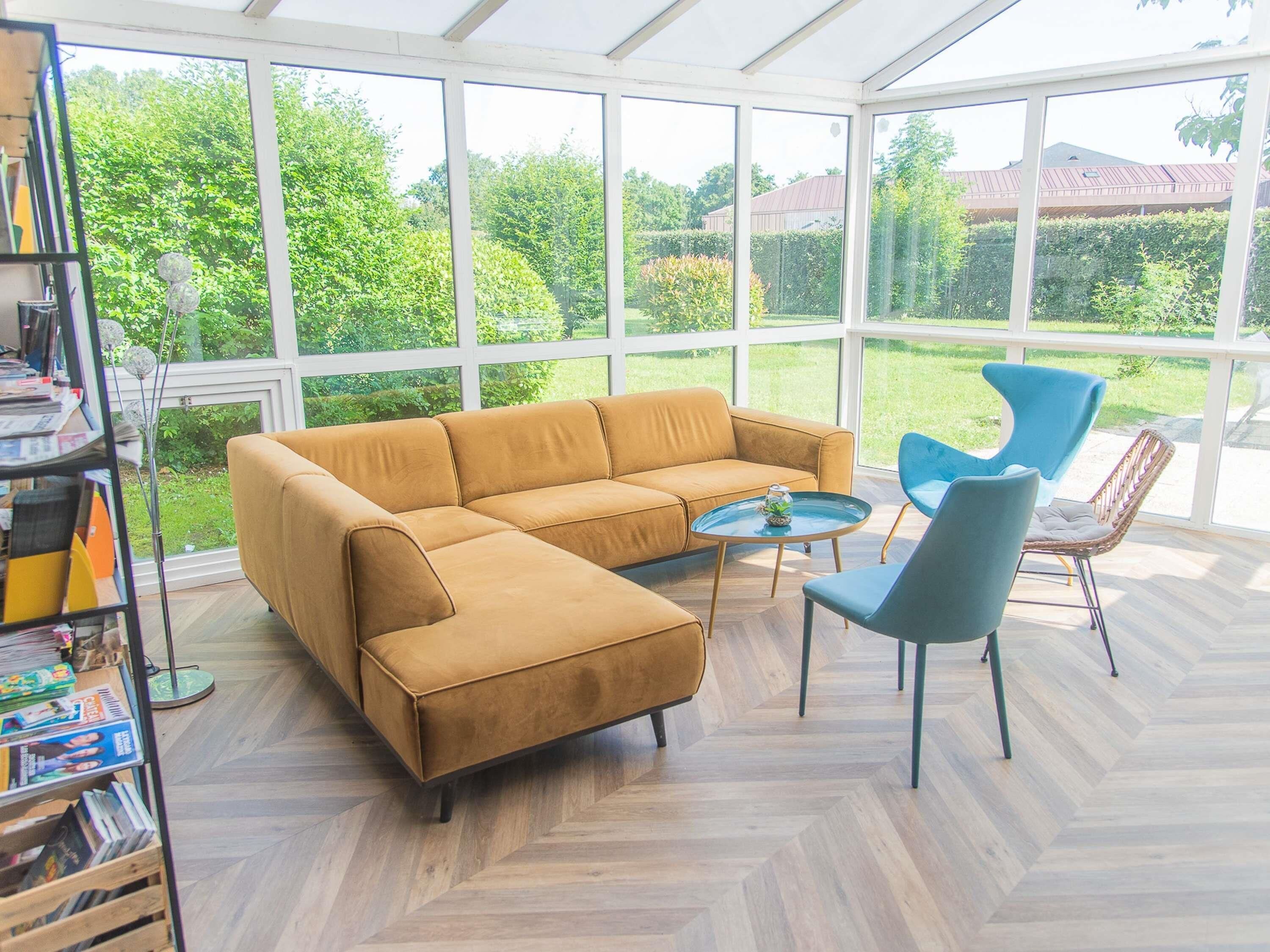 A conservatory with a large window, a sofa, a round coffee table, and two chairs.
