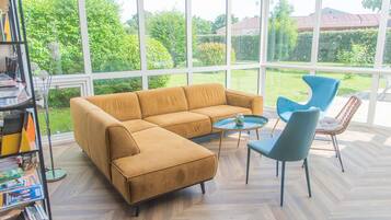 A conservatory with a large window, a sofa, a round coffee table, and two chairs.