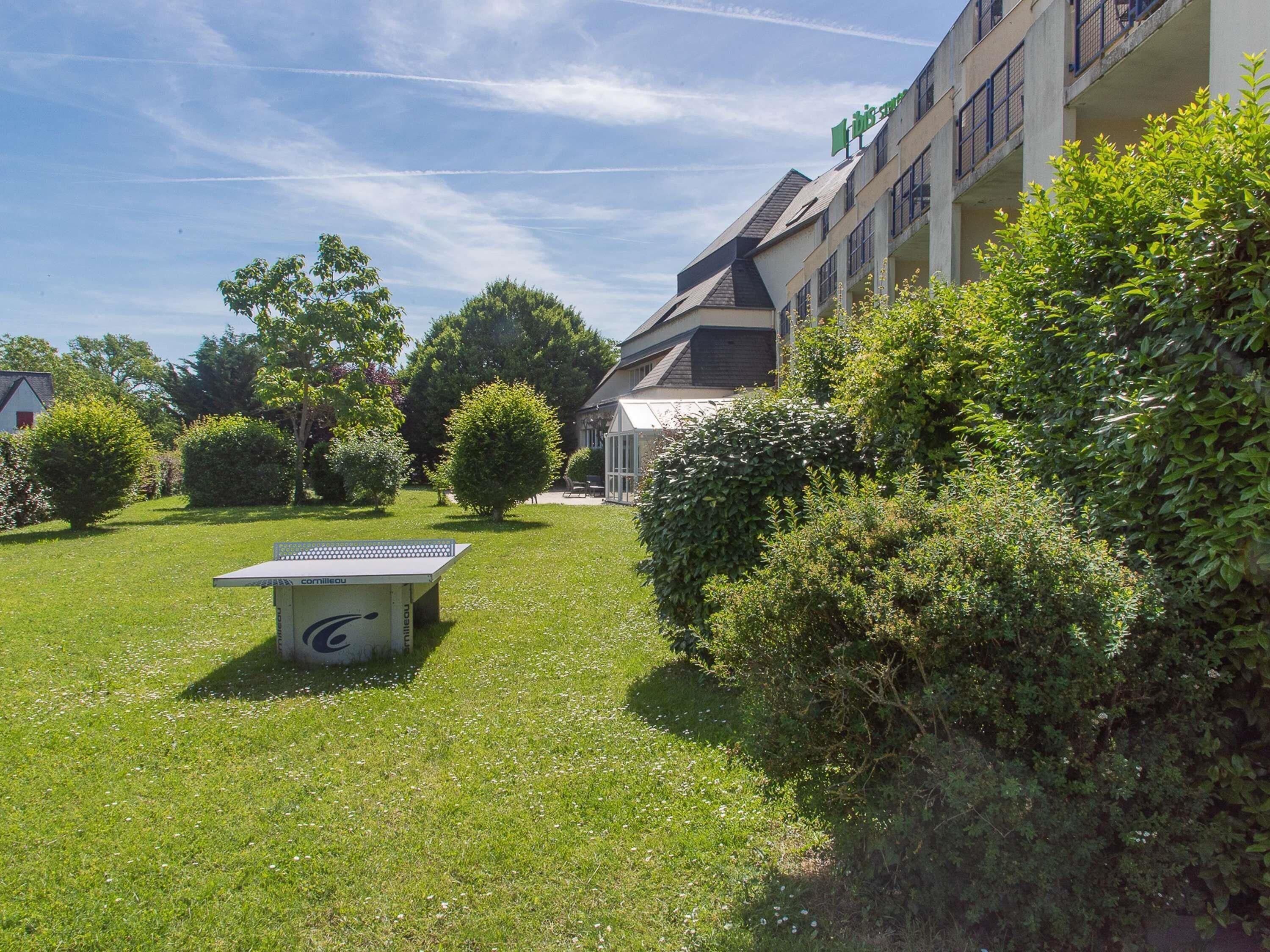 A courtyard with a solar-powered charging station, surrounded by well-maintained grass and hedges, and a building with balconies in the background.