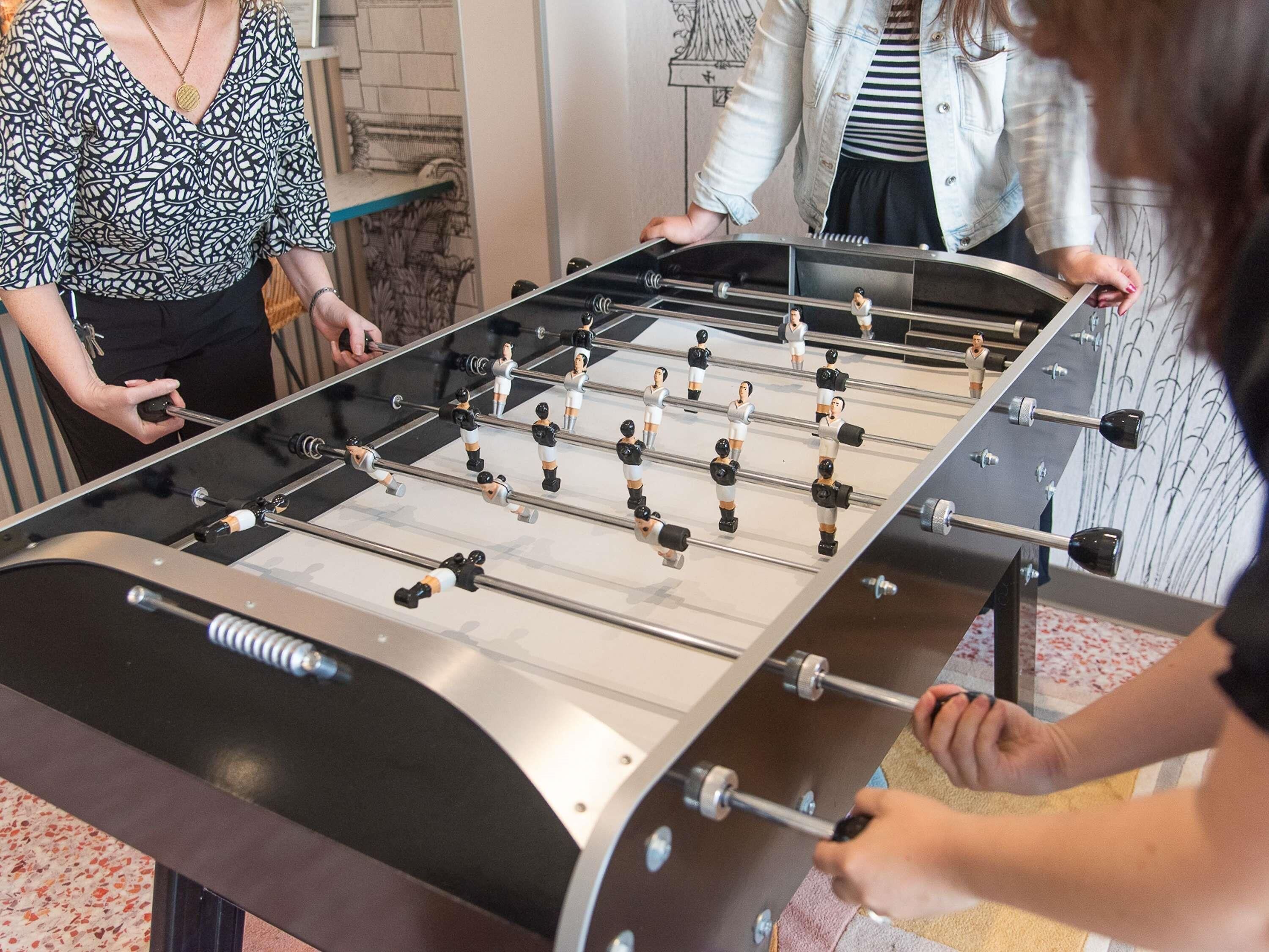 A foosball table with players, a wall with a decorative design, and a person holding a camera.