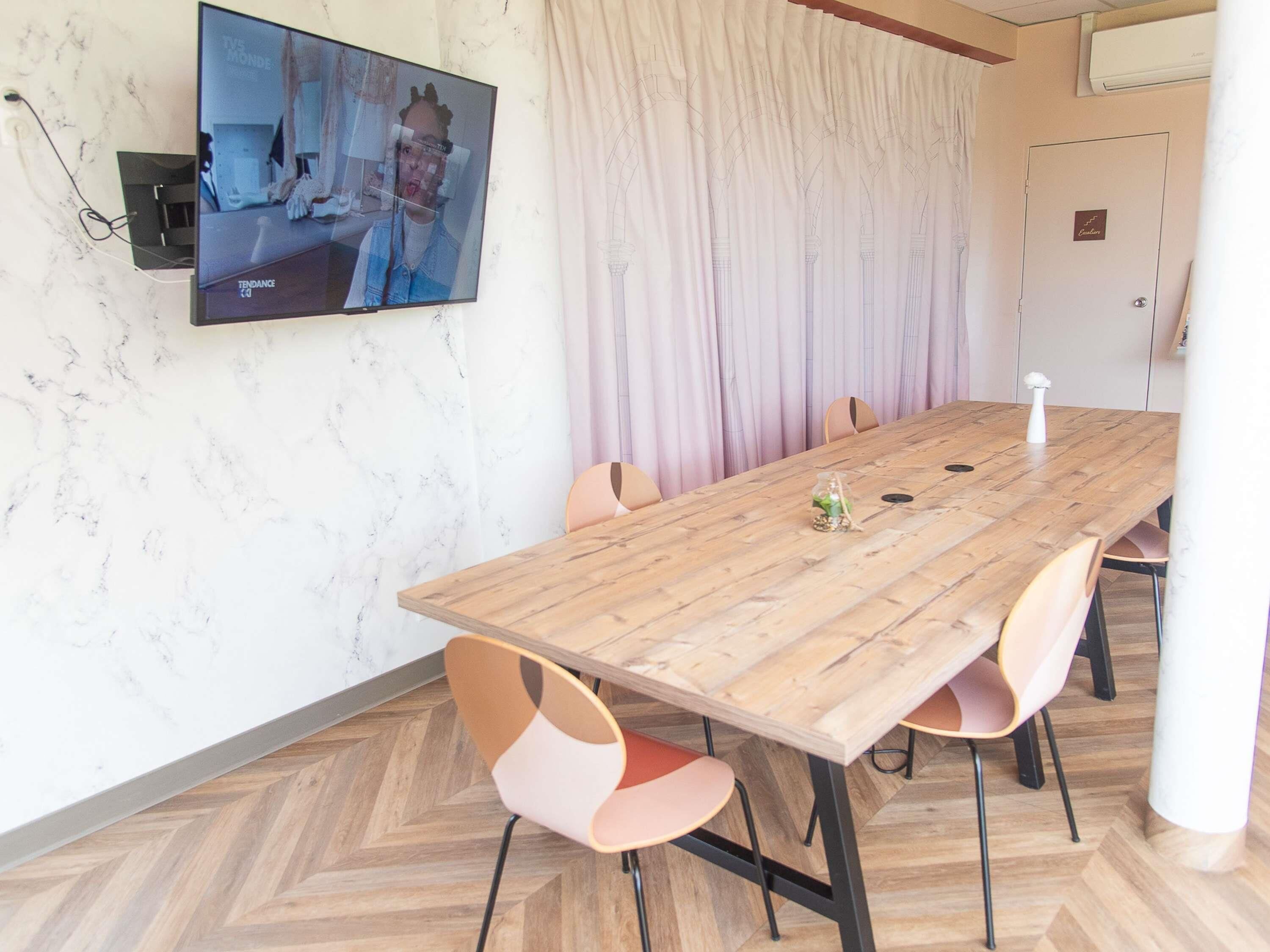 A conference room with a wooden table, six chairs, a television mounted on the wall, and a curtain.
