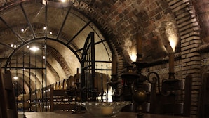 A dimly lit room with a long table and chairs, brick walls, and a vaulted ceiling.