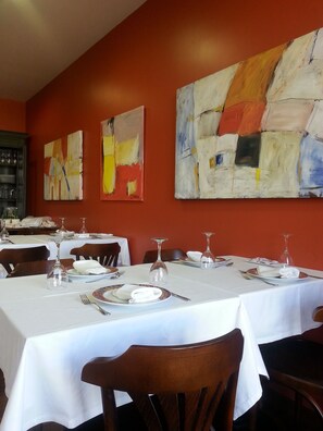 Un restaurant où les tables sont dressées pour le service, et où les murs sont ornés de peintures abstraites.