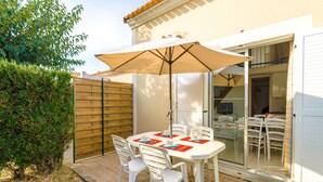 Un patio con una mesa, sillas y una sombrilla, y un ventanal corredero que da a un espacio interior.