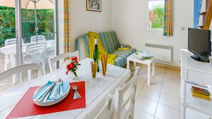 Un salón luminoso con comedor, un sofá, un televisor y una ventana con cortinas.