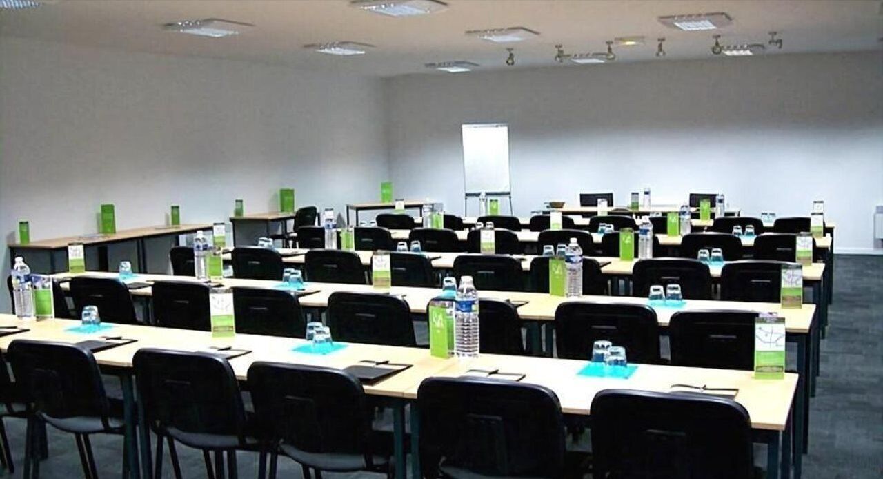 Un salón de conferencias con filas de mesas y sillas, equipado con botellas de agua y tarjetas de identificación.