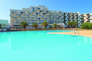 A modern hotel with a large pool, multiple balconies, and palm trees. - Résidence Lagrange Vacances Le Lydia Playa (Le Barcares)