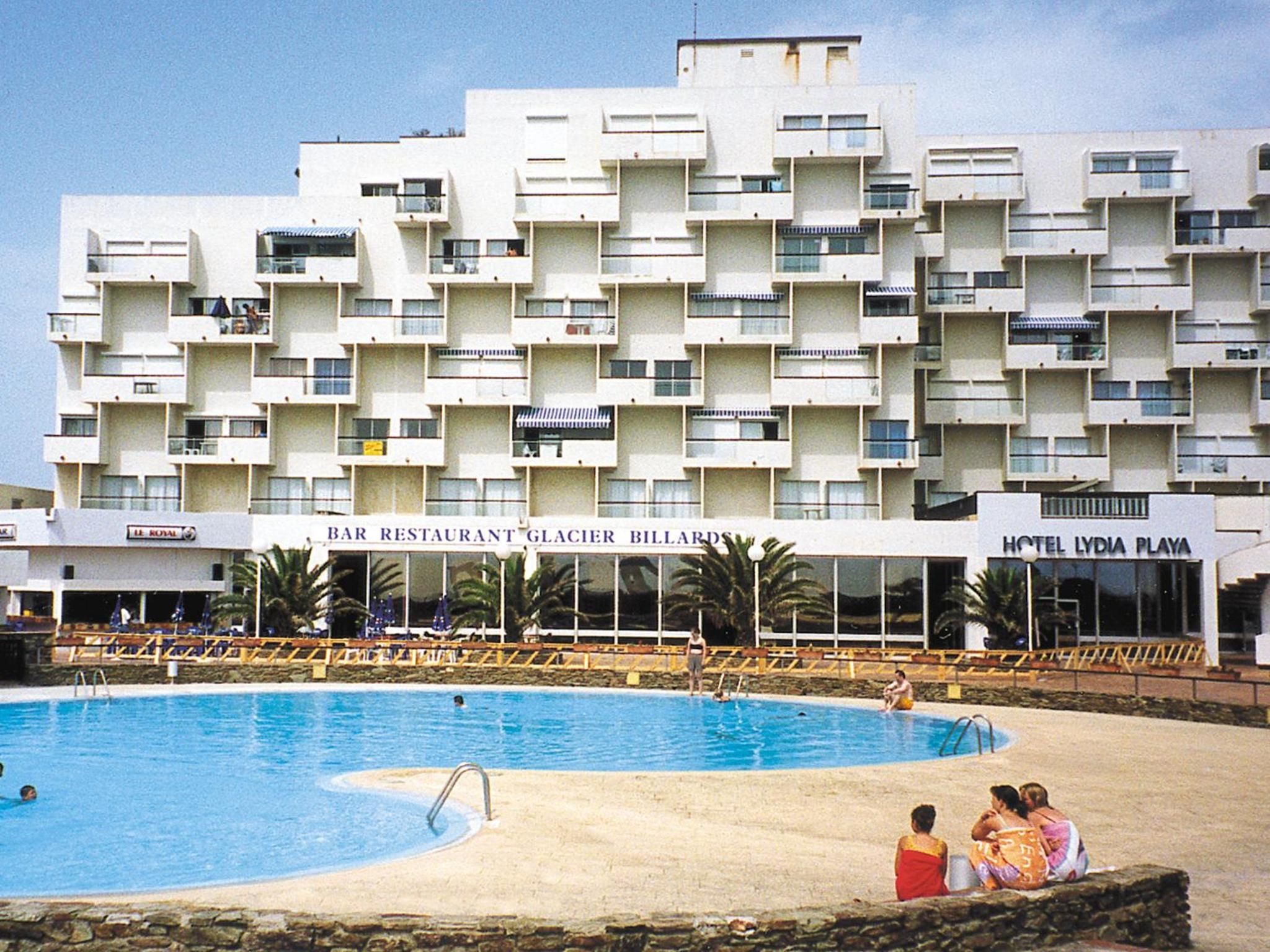 A hotel with a swimming pool, multiple balconies, and a bar restaurant.