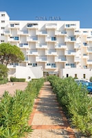Un hotel moderno con un cartel que dice 'EXOTICA PLAYA' en la fachada. Presenta un diseño simétrico con balcones y una entrada central.