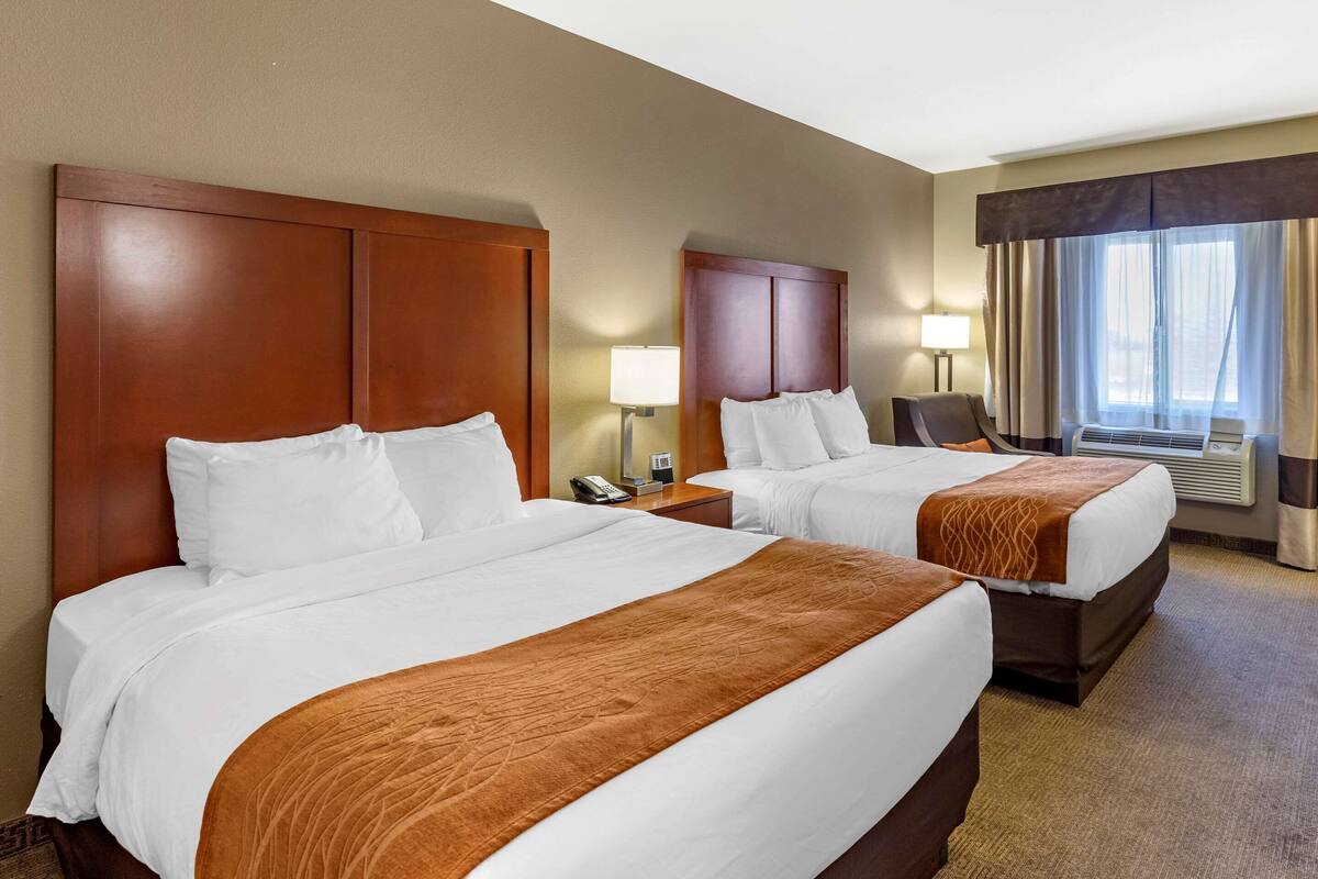 A hotel room with two beds, a desk, a chair, a lamp, and a window with curtains.