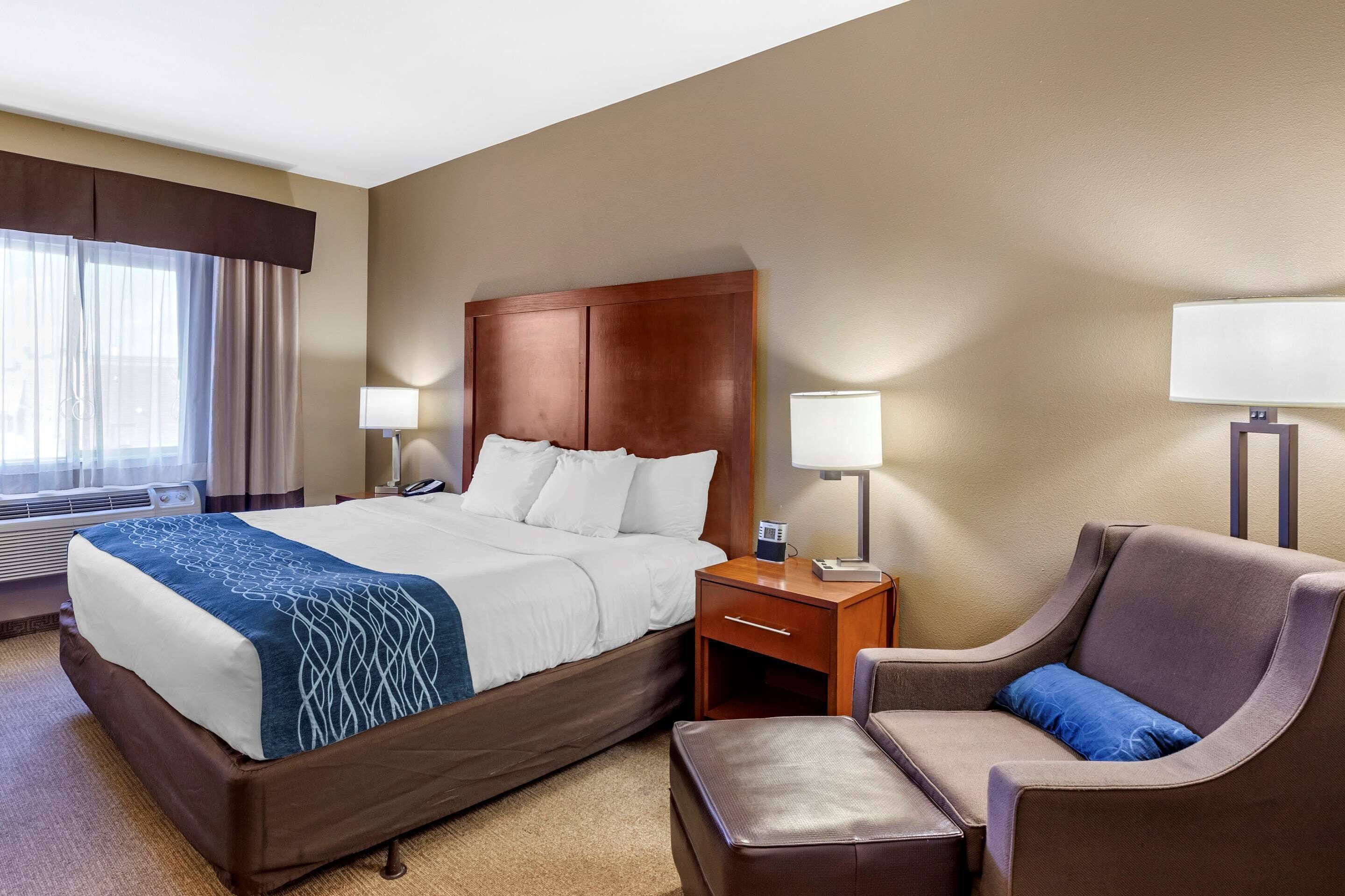 A hotel room with a large bed, bedside tables with lamps, a chair, and a small table.