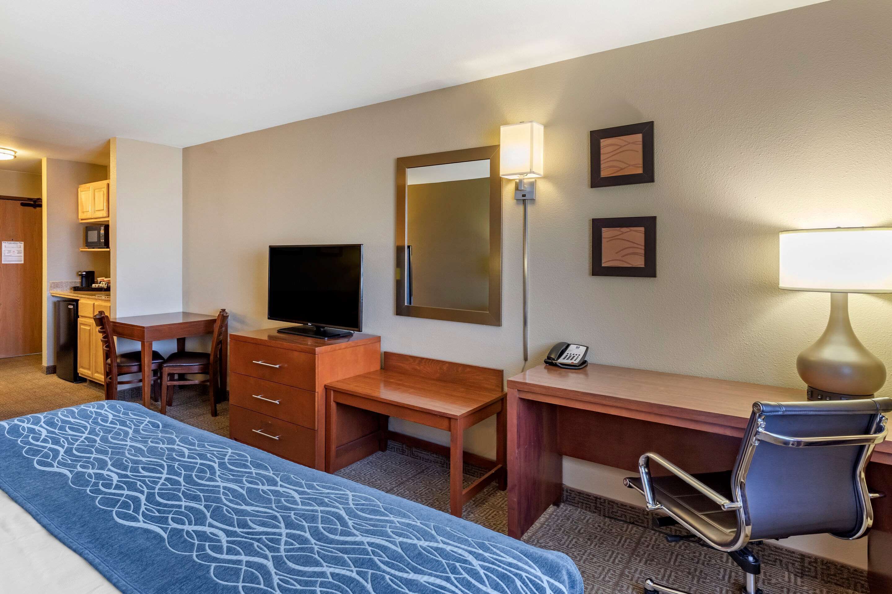 A hotel room with a bed, a desk, a chair, a television, a mirror, and a lamp.