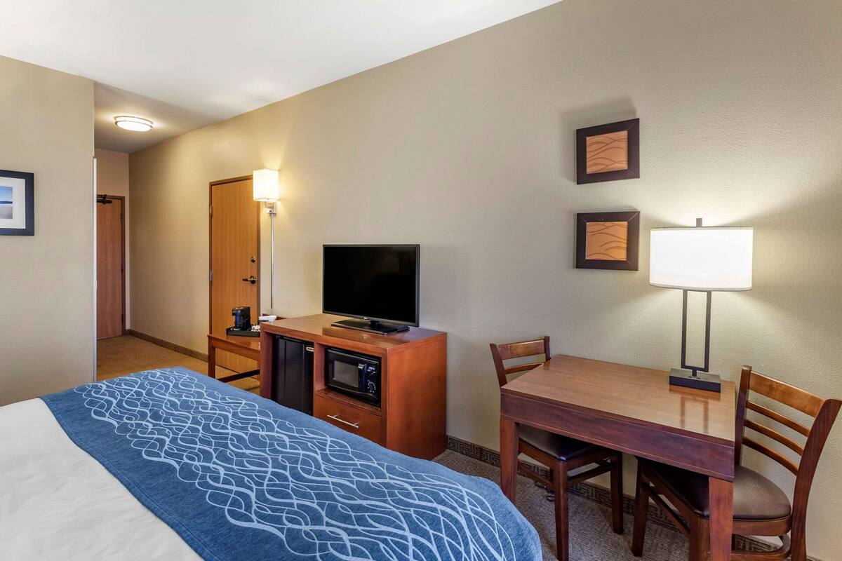 A hotel room with a bed, a desk with a lamp, a television, a microwave, and a door.
