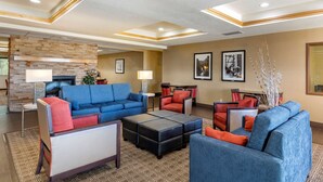 A modern hotel lobby with a stone fireplace, blue sofas, red chairs, and a patterned rug. - Comfort Inn Evansville - Casper (Evansville)