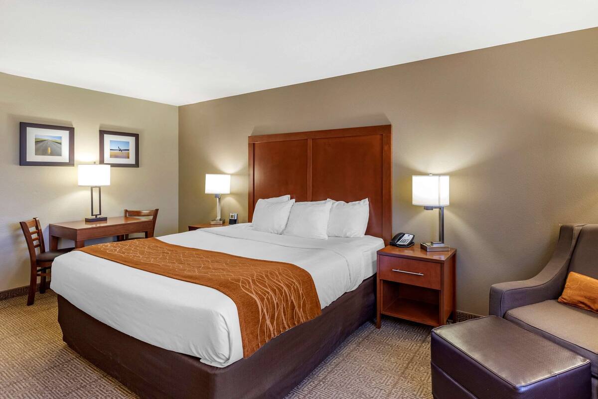 A hotel room with a large bed, two bedside tables with lamps, a desk with a chair, and a small armchair.