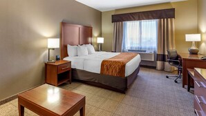 A hotel room with a large bed, two bedside tables with lamps, a desk with a chair, and a view of the city through the window. - Comfort Inn Evansville - Casper (Evansville)